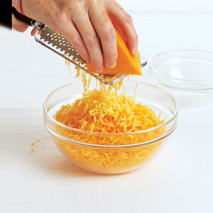 Grating real cheddar cheese into glass bowl