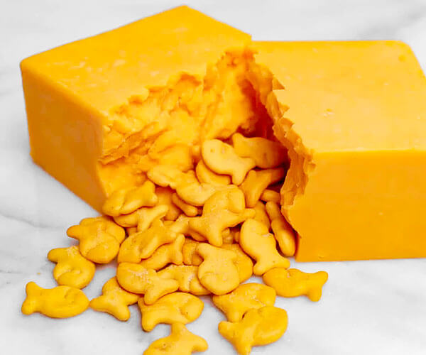 Block of cheddar cheese split open with Goldfish® crackers pouring out