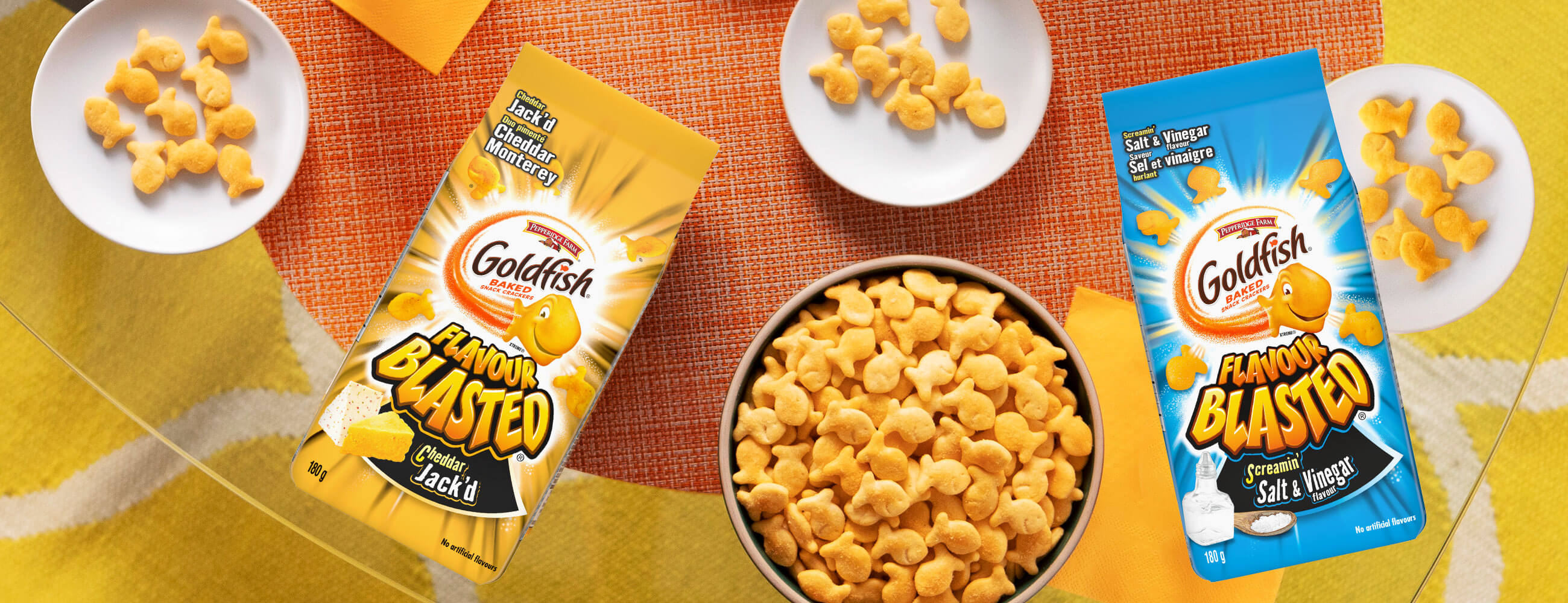 Goldfish® Flavour Blasted® Cheddar Jack'd and Screamin' Salt & Vinegar on table with bowls of Goldfish® crackers